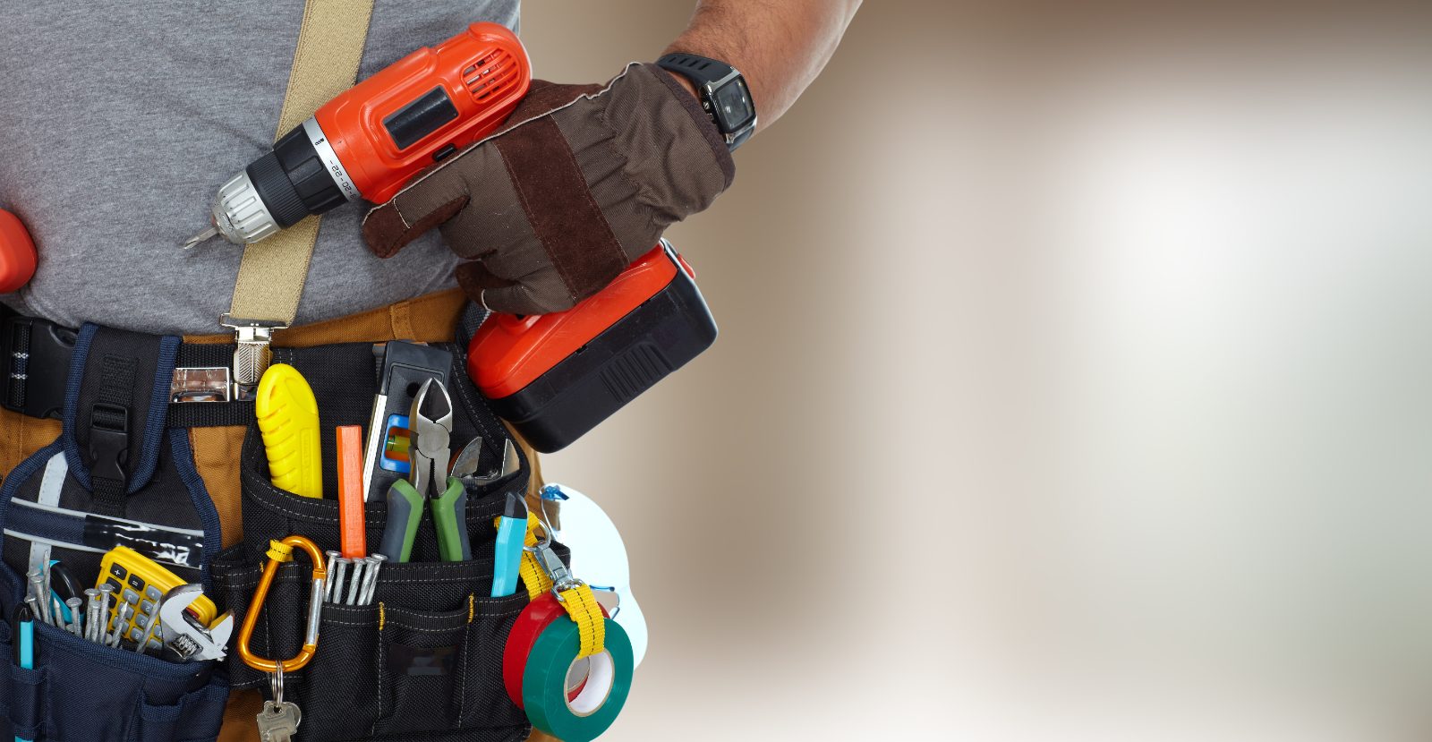 Construction worker wearing tool belt with drill, pliers, tape measures, and other equipment