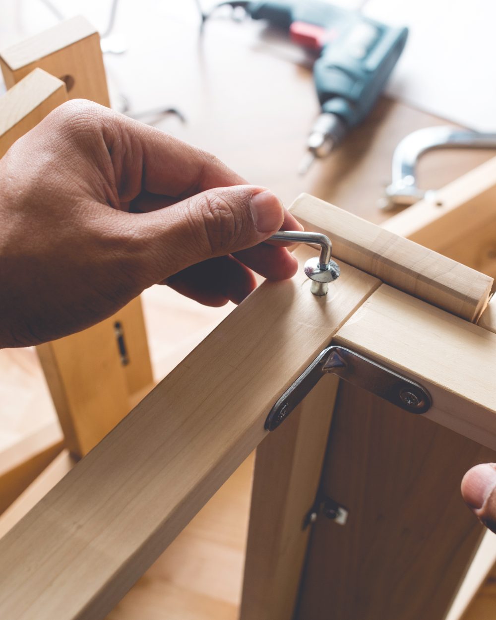 Person installing a metal screw into wooden furniture during assembly