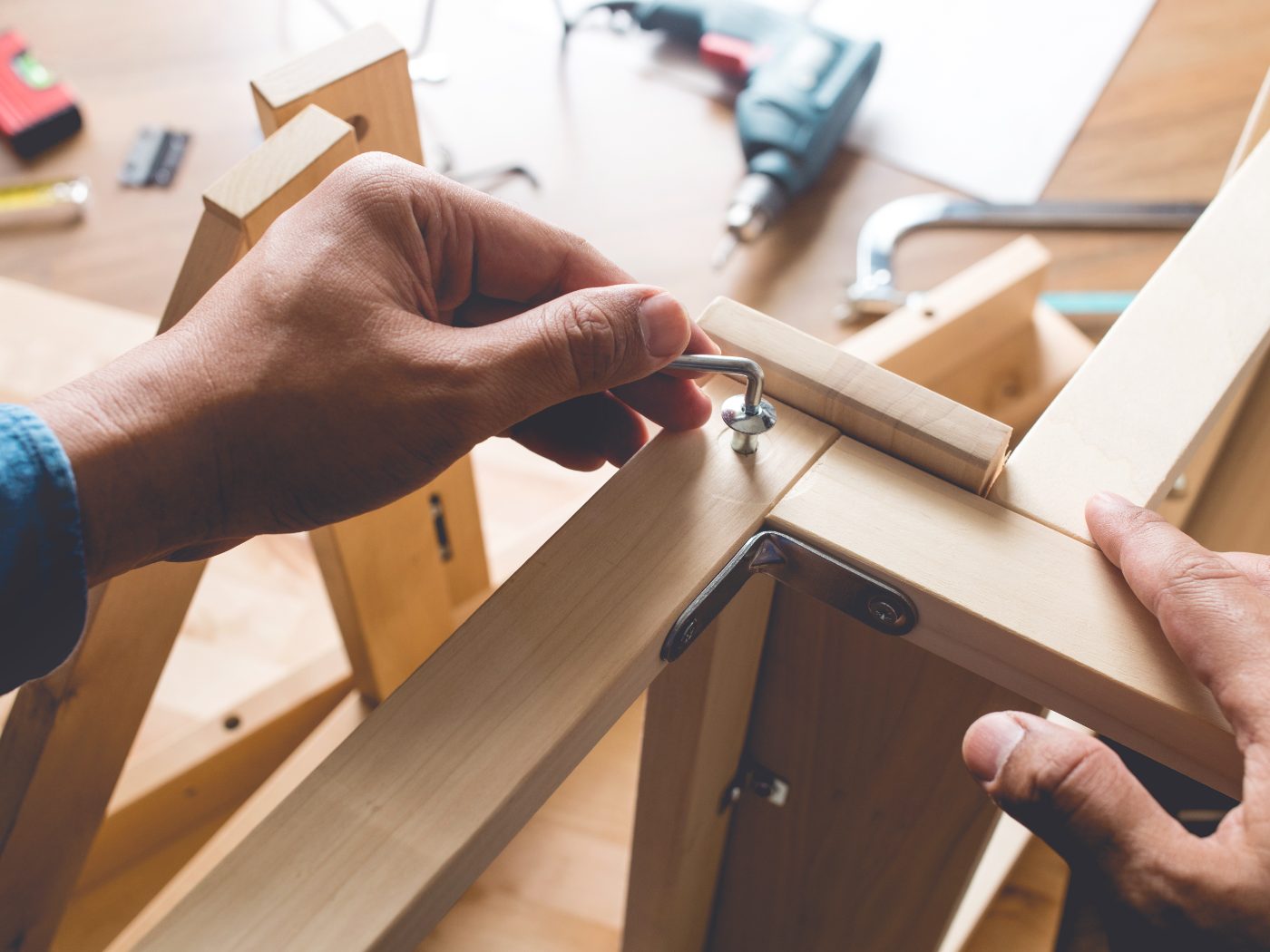 Craftsperson installing a metal hinge on wooden furniture at workbench