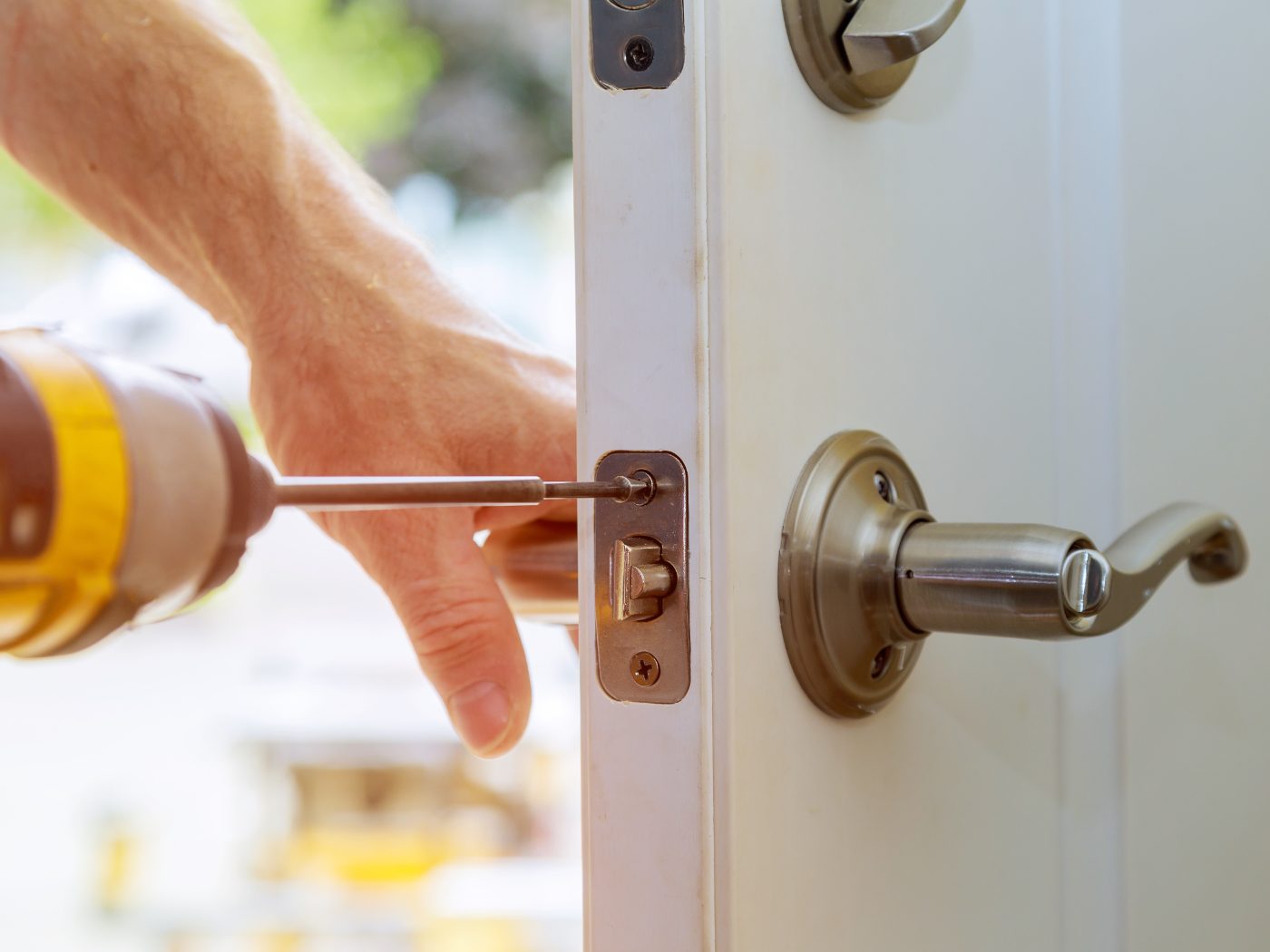 Technician using screwdriver to install door lock hardware on white door frame