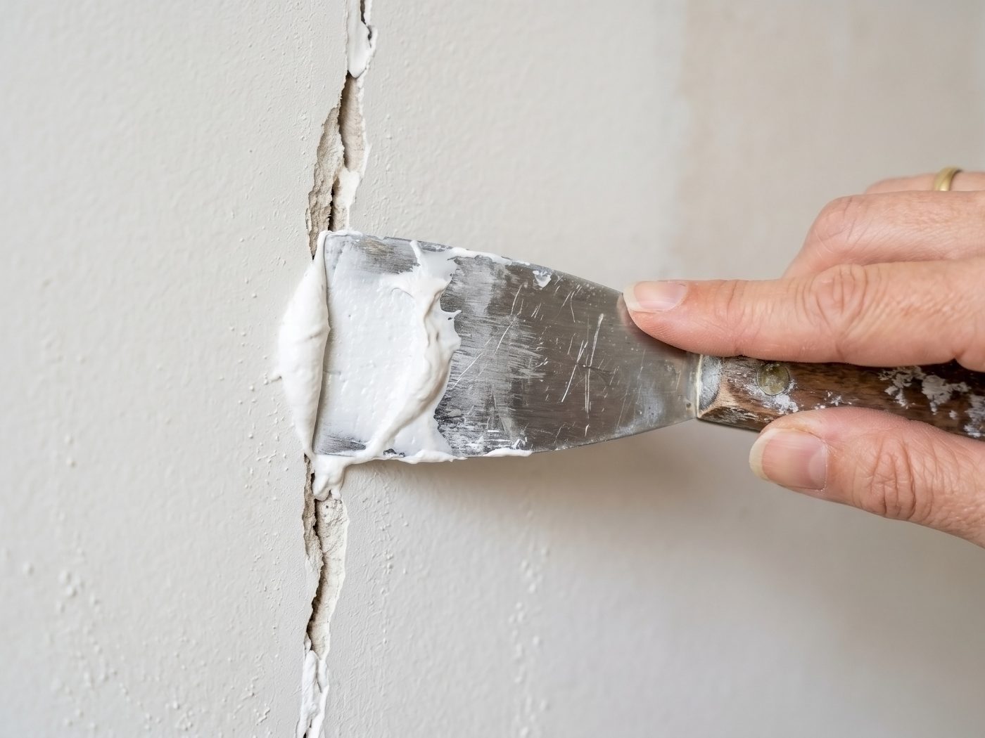 Person applying white spackling compound to a drywall crack with a putty knife