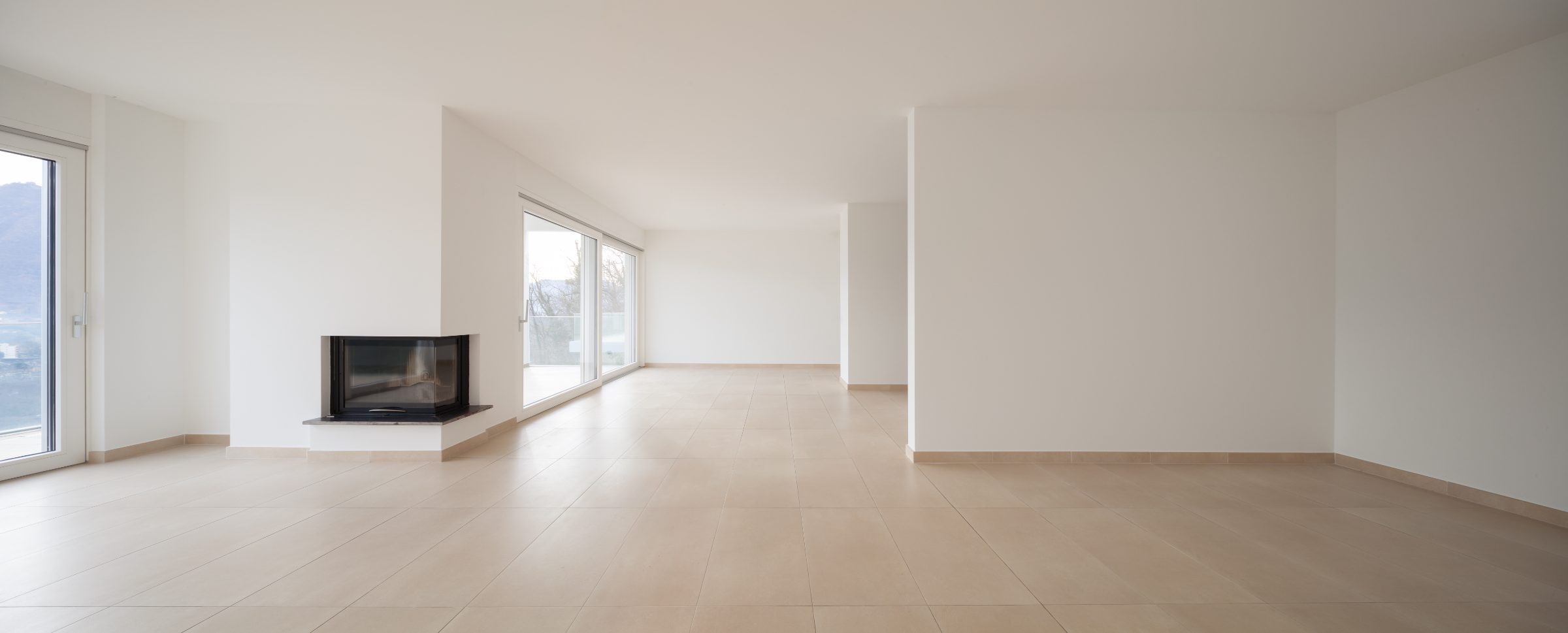 Modern empty living room with light tile flooring, white walls, fireplace, and large windows