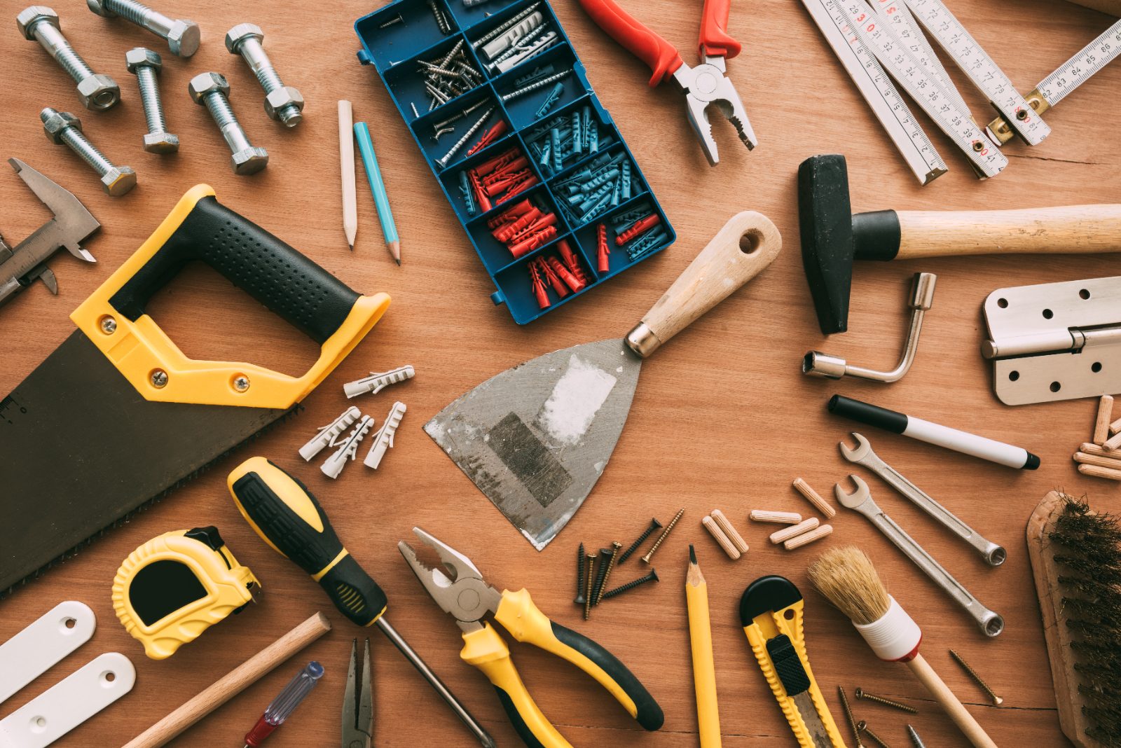 Organized collection of hand tools and hardware including hammers, wrenches, pliers, tape measures, screws, and nails on wooden surface