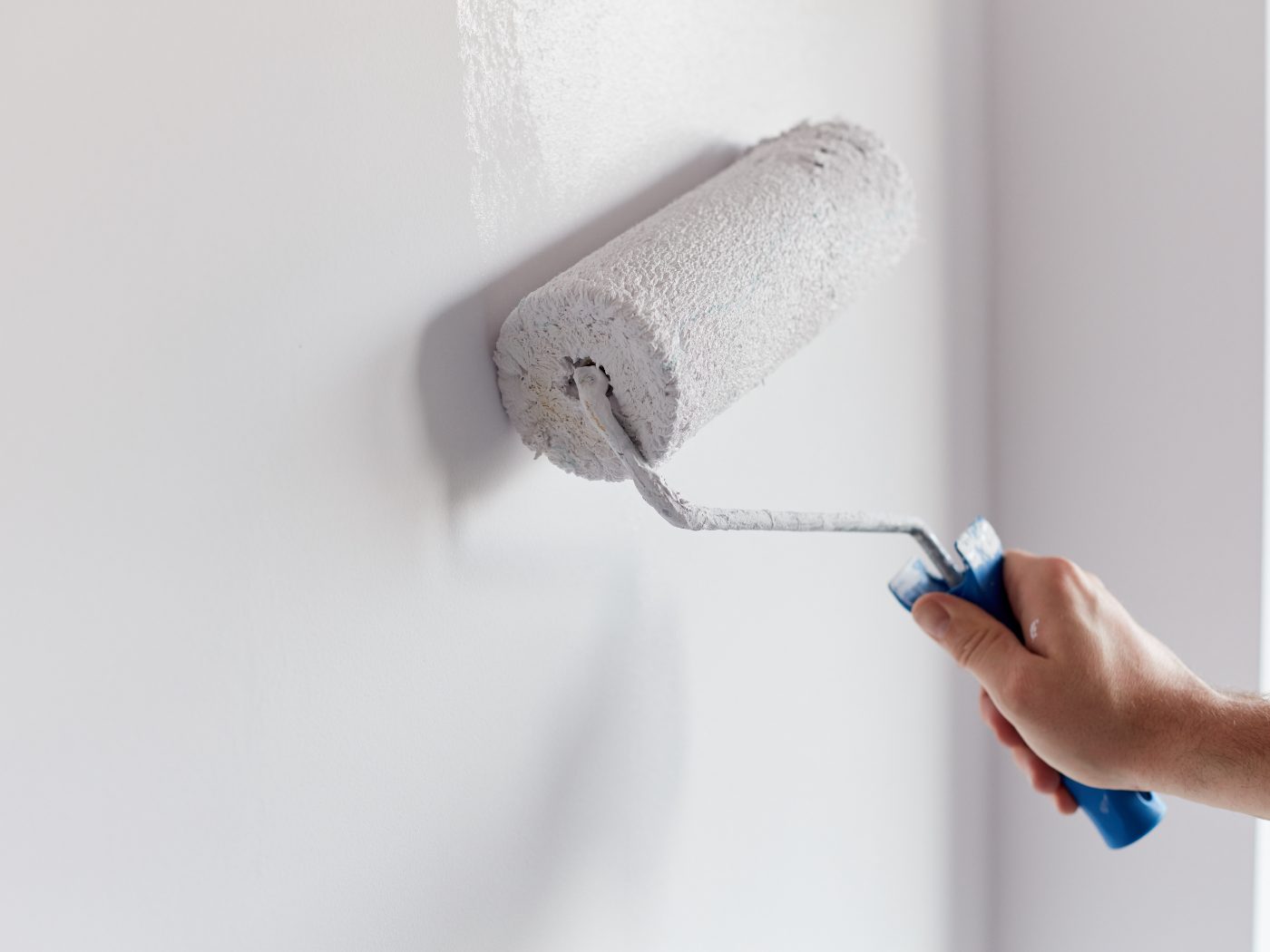 Person holding paint roller with white paint against wall